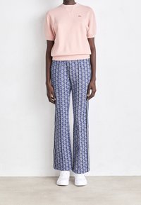 Różowy sweter z krótkim rękawem, wykonany na drutach, zestawiony z niebieskimi szerokimi spodniami w wzory z bocznymi paskami oraz białymi trampkami. Prosty i nowoczesny design.