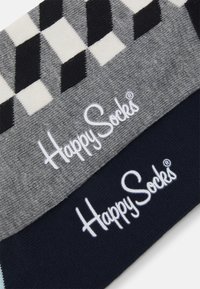 Happy Socks, deux paires de chaussettes ; une grise avec un motif géométrique, l'autre unie bleu marine. Chacune arbore "Happy Socks" brodé en blanc.