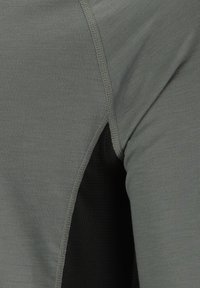 Nærbillede af sømmen under ærmet på en grå langærmet skjorte, der viser et sort, åndbart meshstofpanel.