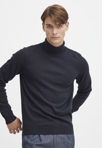 Mørk marineblå strikket turtleneck genser, med ribbestrikket krage og mansjetter, glatt tekstur og tettsittende silhuett. Enkel design uten mønstre.