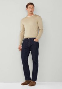 Beżowy sweter z długim rękawem i okrągłym dekoltem, zestawiony z ciemnoniebieskimi dżinsami. Stylizację uzupełniają brązowe sznurowane buty.