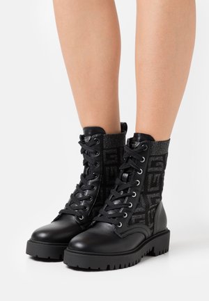 Bottes de combat noires avec un panneau en tissu texturé à motif, corps de chaussure en cuir, bout rond et semelle épaisse en caoutchouc.