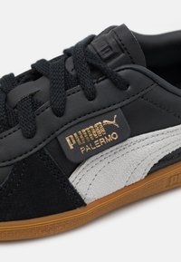 Musta nahka- ja mokkakengät, joissa on harmaa raita ja kultainen "PUMA PALERMO" -logo. Varustettu teksturoiduilla nauhoilla ja kumipohjalla.