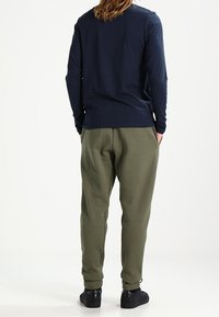 Langärmliges navy Bluse mit Rundhalsausschnitt, kombiniert mit olivgrünen Jogginghosen. Die Hosen haben elastische Bündchen; das Outfit umfasst schwarze Sneakers.