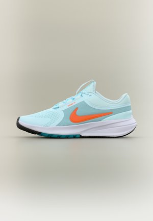 Chaussure de sport bleu clair avec le logo Nike orange, semelle blanche et dessous à crampons noirs, vue de côté sur un fond uni.
