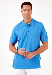 Polo de manga corta en azul brillante, hecho de una tela suave, con cuello y tapeta de tres botones, y un corte relajado.