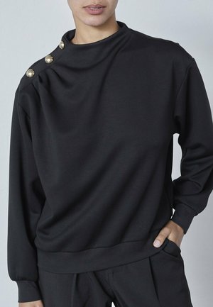 Sort sweatshirt med høj hals, lange ærmer og tre dekorative guldknapper på skulderen. Blød, glat stof med en afslappet pasform.