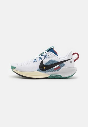 Chaussure de trail Nike blanche avec swoosh noir, accents bleus et rouges, semelle beige et semelle extérieure verte sur fond blanc.