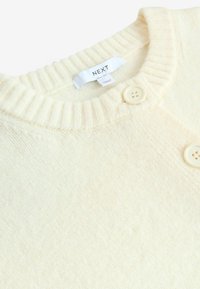 Crème-kleurige gebreide trui met een geribde kraag, voorzien van twee grote, lichte knopen en een zachte textuur. Merklabel zichtbaar.