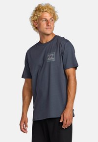 Dark gray cotton t-shirt with short sleeves, featuring a small logo graphic on the left chest. Simple, relaxed fit design, smooth texture.