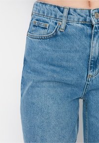 Jeans de mezclilla azul con cintura alta, diseño clásico de cinco bolsillos y detalles de costura visibles. La tela parece ligeramente texturizada.