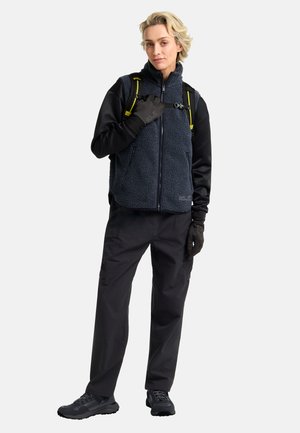 Dark fleece vest with zip closure over a long-sleeve black top, paired with black pants and gloves, complemented by a yellow-accented backpack.