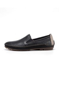 Zapatos negros sin cordones con parte superior de cuero perforado, tacón gris en contraste y detalle de costura beige a lo largo de la suela. Suela de goma plana.
