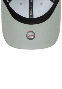 Parte inferior de una gorra de béisbol gris que muestra una etiqueta de autenticidad redonda de la MLB con un gráfico de costura roja y un número de serie en el visera.