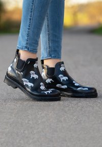 Black rubber ankle boots with a glossy finish, featuring a white dog print. The boots have elastic side panels and a textured sole.