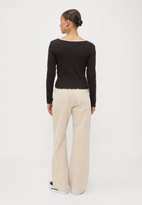 Black long-sleeve top with scalloped hem paired with wide-leg beige pants; features a low back neckline and minimalistic design elements.