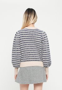 Gestrickter Pullover mit puffierten Ärmeln, der ein navy- und cremefarbenes Karomuster zeigt. Rippenbündchen und -saum, von hinten gezeigt.
