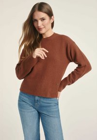 Brązowy sweter z dzianiny z prążkowanym dołem i mankietami, z okrągłym dekoltem. W połączeniu z jasnoniebieskimi dżinsami.