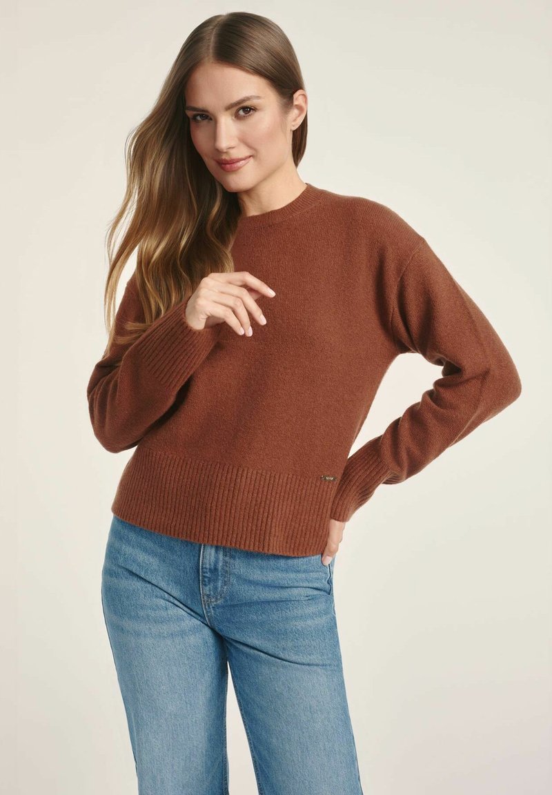 Brązowy sweter z dzianiny z prążkowanym dołem i mankietami, z okrągłym dekoltem. W połączeniu z jasnoniebieskimi dżinsami.