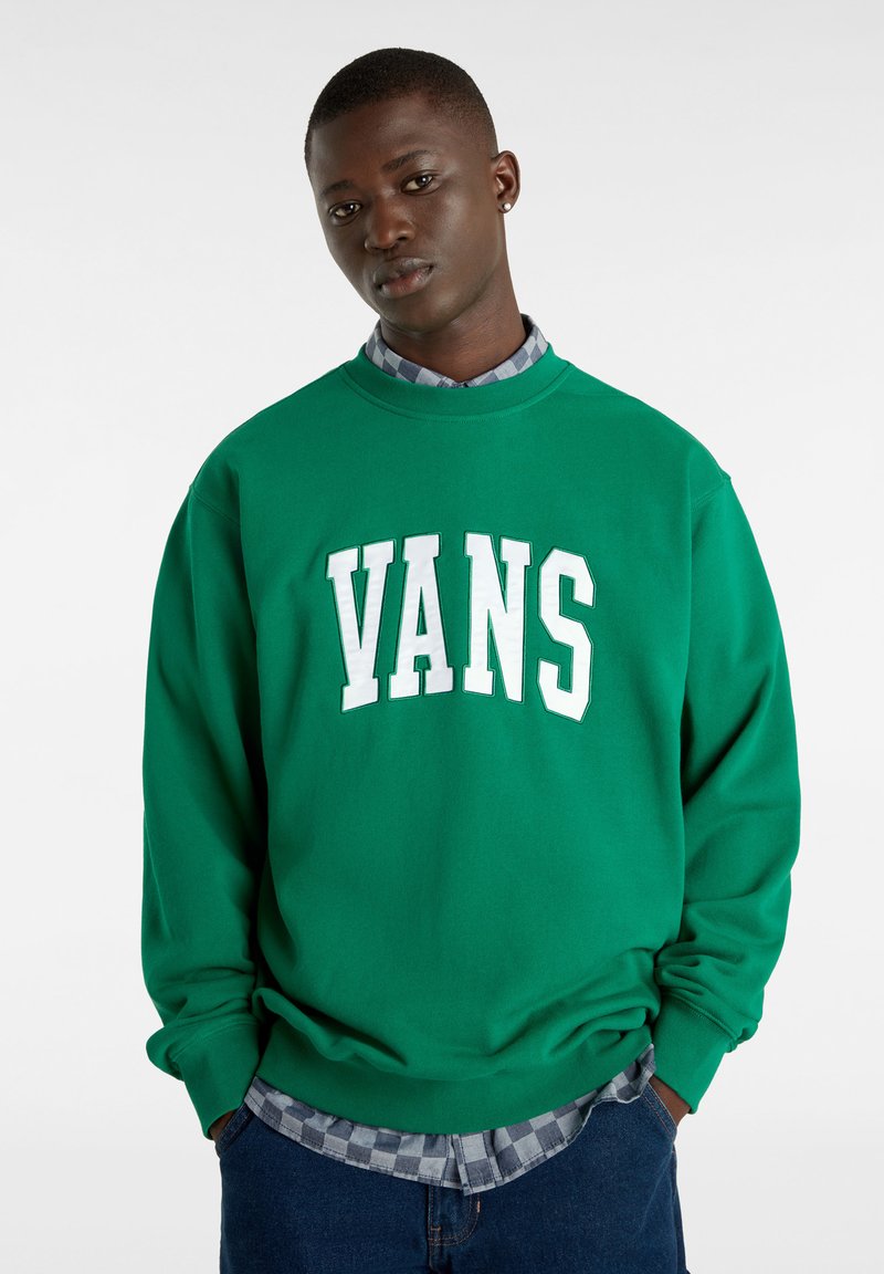 Sudadera verde con el logo blanco de "VANS", diseño de cuello redondo, material de algodón y mangas texturizadas, usada sobre una camisa de cuadros.