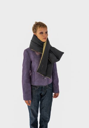 Sort tørklæde med gul kant, lavet af et blødt materiale, viklet om halsen. Modellen bærer en lilla jakke og blå jeans.