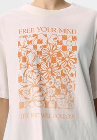 Camiseta de algodón blanca con mangas cortas que presenta un gráfico floral naranja y el texto: "LIBERA TU MENTE" arriba y "LO DEMÁS SE SEGUIRÁ" abajo.