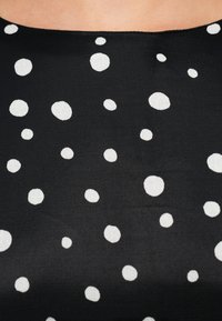 Schwarzer Stoff mit glatter Textur, versehen mit unregelmäßigen weißen Punkten in verschiedenen Größen und einem tief ausgeschnittenen Halsausschnitt.