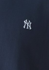 Mornarski pamučni majica u mornarsko plavoj boji sa malim bijelim vezom logotipa New York Yankees na lijevoj strani prsnog koša. Glatka tekstura, ležeran dizajn.