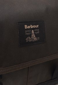 Zwarte stoffen tas met een gestikt Barbour merklabel, waarop een vuurtoren en golven zijn afgebeeld in lichtbruine draad.