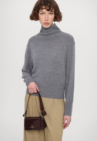 Grå strikket turtleneck genser med lange ermer, brukt med beige bukser. Modellen holder en liten burgunder håndveske med glanset finish og stropp.