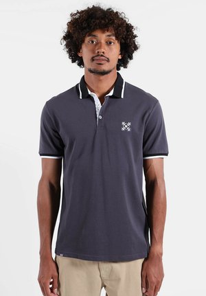 Polo gris foncé avec un col blanc, des accents noirs et un motif de flocon de neige sur le côté gauche de la poitrine. Manches courtes avec détails de bordure.