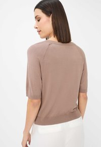 Brun kortærmet striktrøje med rund halsudskæring, ribbede kanter og let cropped design, båret med hvide bukser.