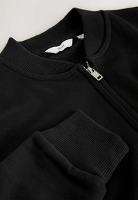 Giacca nera con zipper, caratterizzata da colletto e polsini a coste, tessuto liscio e dettaglio della cerniera argentata sul davanti.