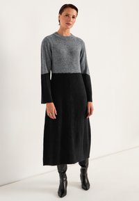 Neulosmekko, jossa on pitkät hihat, harmaa yläosa ja musta alaosa, valmistettu pehmeästä, teksturoidusta kankaasta. Yksinkertainen pyöreä pääntie ja suora malli.