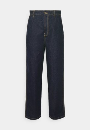 Jeans de mezclilla oscuros de pierna ancha con costuras amarillas, que cuentan con un cierre frontal de botón y bolsillos laterales. Textura suave y diseño tradicional.