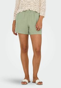 Lichtgroene shorts met een elastische tailleband, gemaakt van zachte stof. Gecombineerd met een crèmekleurig gehaakt topje en platte witte sandalen.