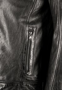 Detail van een zwarte leren jack met een ritsvak, een metalen rits, een gladde textuur en zichtbare stiksels langs de naden.