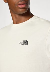Cream-colored cotton T-shirt featuring a round neckline and a small black logo of "The North Face" on the left chest area.