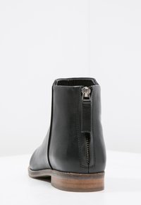 Czarne skórzane botki za kostkę z okrągłym noskiem i zamkiem błyskawicznym z tyłu; mają lekko podniesiony, drewniany obcas i gładką fakturę.
