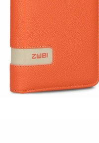 Coin de un portefeuille texturé orange avec une étiquette en tissu beige cousue, affichant le nom de la marque "zwei" en texte orange.