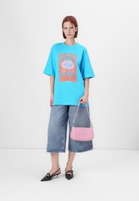 Svetlo modra oversize majica z grafičnim potiskom, v kombinaciji z širokimi denim culotami. Drži majhno roza torbico; črne špicaste balerinke.