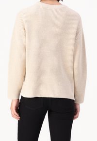 Jersey de punto en color crema, con textura acanalada, hombros caídos y corte holgado. Estilo pulóver con escote redondeado.