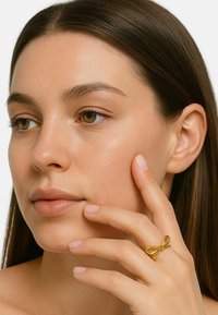 Goldring, gestaltet wie eine Schleife, mit glatter Metalloberfläche und minimalistischen Stil. Das Modell hält den Ring an ihrem Finger und präsentiert seine Form und seinen Glanz.
