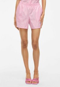 Różowe szorty w paski z elastyczną talią. Gładki materiał o luźnym kroju, sięgający do połowy uda. Połączone z różowymi sandałami na obcasie.