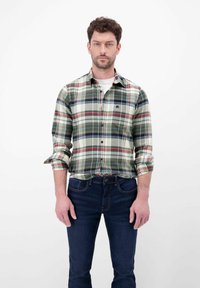 Zielona i kremowa koszula w kratę z czerwonymi i niebieskimi akcentami, z kołnierzykiem zapinanym na guziki, z podwiniętymi rękawami, noszona z ciemnoniebieskimi dżinsami. Gładka tekstura materiału.