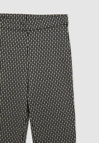 Pantalon à motifs noir et blanc en tissu lisse et texturé. Le design présente des lignes verticales et des points sur la surface. Ceinture large.