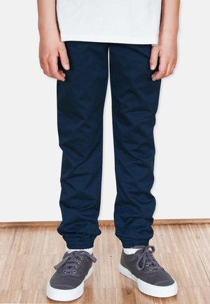 Marineblaue Jogginghosen mit elastischen Bündchen, aus leichtem Material gefertigt. Getragen mit grauen Turnschuhen mit weißen Sohlen und Schnürdetails.