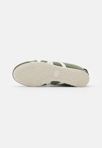 Zapatillas verdes con acentos blancos, suela de goma con un patrón de agarre texturizado y un diseño de perfil bajo.