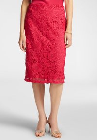 Gonna a matita rossa in pizzo con motivi floreali, tessuto testurizzato, lunghezza a metà polpaccio e orlo scallop. Abbinata a tacchi alti con cinturini.