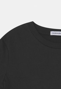 Černé bavlněné tričko s kulatým výstřihem a krátkými rukávy. Štítek označuje "Calvin Klein." Hladká textura s minimálním švem.